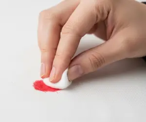 نمای نزدیک از لکه لاک قرمز روی لباس سفید و پنبه آغشته به استون