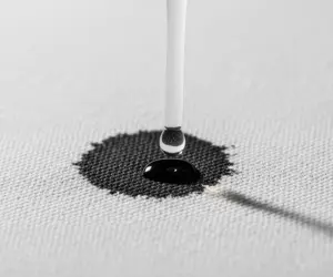 نمای نزدیک از قطره حلال تخصصی در حال اثر بر لکه جوهر روی پارچه؛ نماد راهکارهای حرفه‌ای برای لکه‌های سخت.