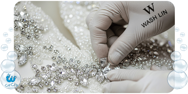 دست متخصص واشلین در حال محافظت از سنگدوزی لباس عروس قبل از خشکشویی، نماد مراقبت از تزئینات.