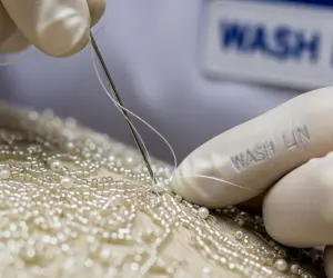 تصویر ماکرو از دست متخصص واش‌لین در حال ترمیم سنگ‌دوزی یک لباس مجلسی، نماد خشکشویی تخصصی لباس‌های مجلسی.